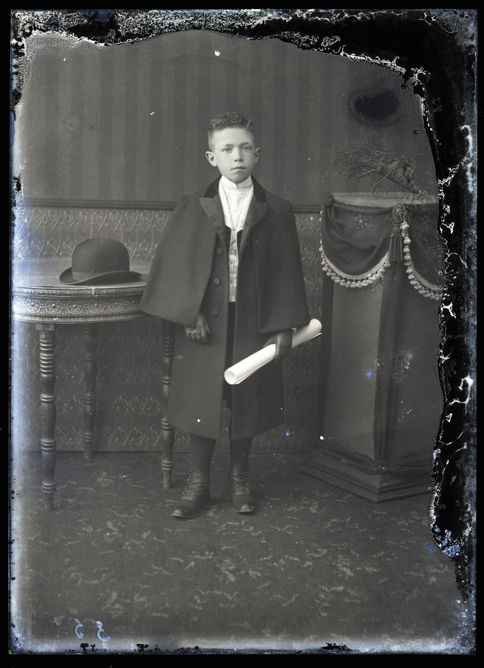 Staand portret van jongeman, feestkledij met lange mantel lederen handschoenen, opgerold dokument in linkerhand, Melle , 1910-1920 | Erfgoedbank Land Van Rode