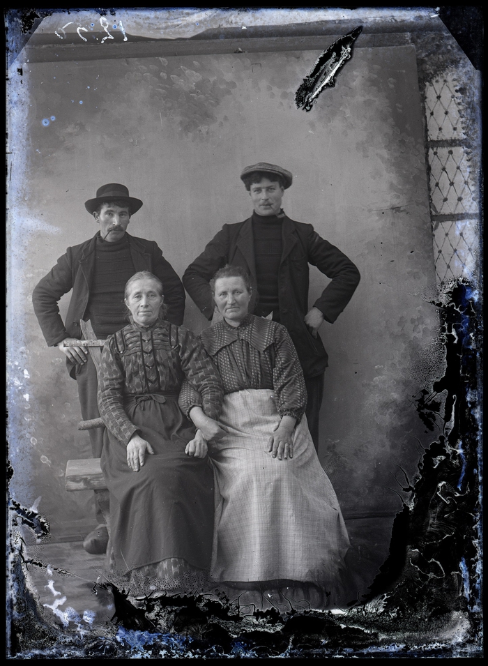 Studiofoto van vrouwen in lange feestkledij en naar achter gekamd haar en 2 mannen in vest en donkere hoogsluitende trui, beiden met een pijp in de één met hoed en