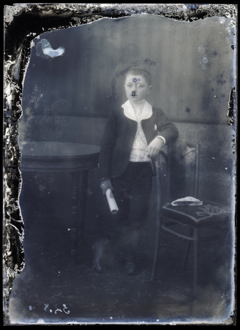 Rechtstaande foto van jongeman in feestkledij met wit hemd en witte kraag, kortgeknipt haar, opgerold document in rechterhand, Melle , 1910-1920