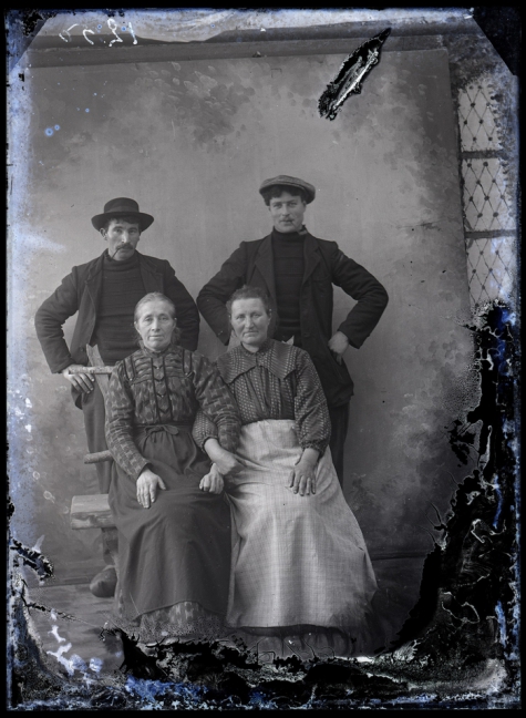 Studiofoto van 2 vrouwen in lange feestkledij en naar achter gekamd haar en 2 mannen in vest en donkere hoogsluitende  trui, beiden met een pijp in de mond, één met hoed en andere met pet, Melle , 1910-1920