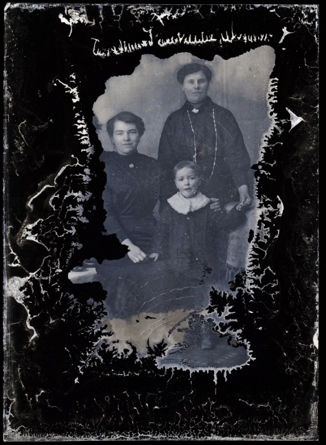 Staand familieportret 3 generaties, grootmoeder met donkere lange kledij en lange halsketting, moeder met opzij gekamd haar, 2 jonge kinderen, Melle , 1910-1920