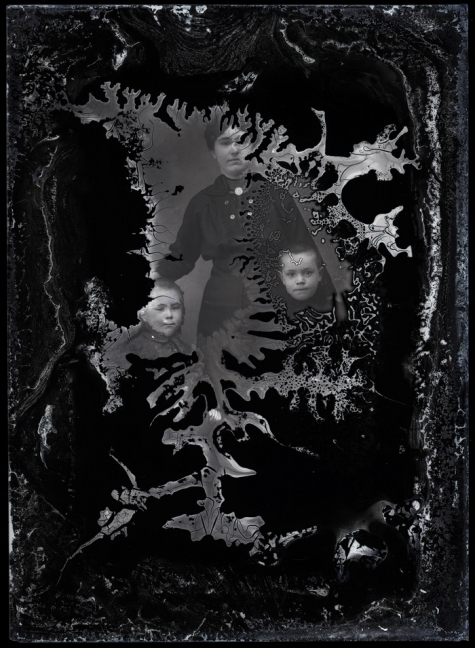 Staand portret van jonge vrouw in donkere feestkledij en borstspeld, met 2 jongentjes met kort geknipt haar, Melle , 1910-1920
