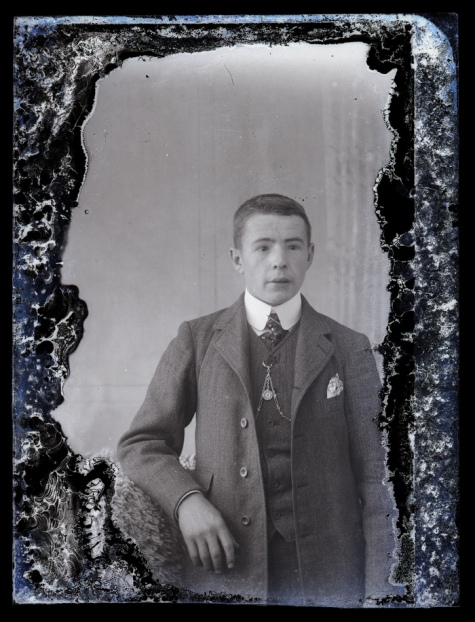 Staande foto van jonge man met kostuum, wit hemd en stropdas, kort geknipt haar, ketting voor borstuurwerk, Melle , 1910-1920
