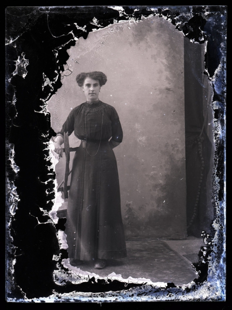 Staand portret van jonge vrouw in lange feestkledij met lange halsketting en golvend gekruld opgestoken haar, Melle, 1910-1920