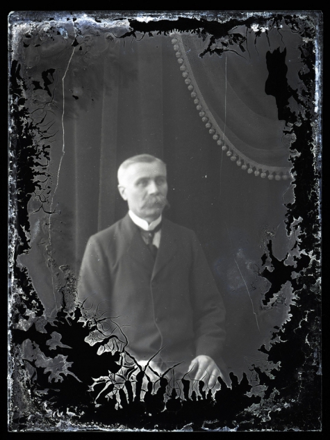 Zittend portret van man in feestkledij met wit hemd en stropdas, gemodelleerde snor en glad naar rechts gekamd haar, Melle, 1910-1920