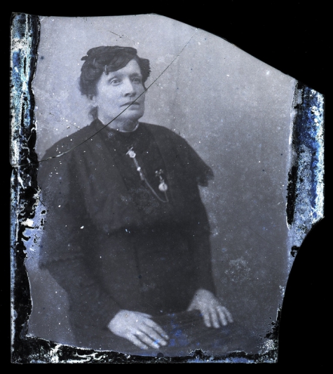 Zittend portret vrouw in donkere feestkledij, opgemaakt haar en borstketting, Melle, 1910-1920