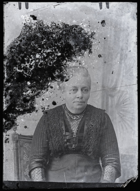 Zittende foto van vrouw in feestkledij bestaande uit rok en vestje met driekwartmouwen, strak naar achter gekamd haar, Melle, 1910-1920