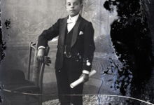 Staand portret, tiener in feestkledij, wit hemd en witte vlinderdas, lederen handschoenen, opgerold document in linkerhand, Melle , 1910-1920