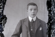 Staande foto van jonge man met kostuum, wit hemd en stropdas, kort geknipt haar, ketting voor borstuurwerk, Melle , 1910-1920