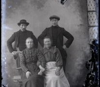 Studiofoto van 2 vrouwen in lange feestkledij en naar achter gekamd haar en 2 mannen in vest en donkere hoogsluitende  trui, beiden met een pijp in de mond, één met hoed en andere met pet, Melle , 1910-1920