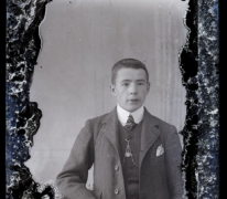 Staande foto van jonge man met kostuum, wit hemd en stropdas, kort geknipt haar, ketting voor borstuurwerk, Melle , 1910-1920