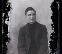 Zittend portret van jongeman in kostuum met halsdichte pullover, kuifvormig gekamd haar met linkerscheiding, Melle , 1910-1920
