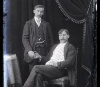 Portret van staande man in feestkledij met wit hemd en stropdas en zittende man, beiden met snor en kuifvormig gekamd haar , Melle , 1910-1920
