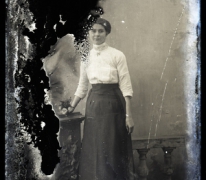 Staand portret van jonge vrouw in feestkledij bestaande uit lange rok en witte bloes met driekwart mouwen, opgestoken haar, Melle , 1910-1920