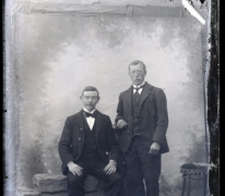 Portret van 1 staande en 1 zittende man in feestkledij zijnde kostuum en wit hemd met stropdas en vlinderdas, Melle , 1910-1920