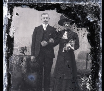 Staand portret van een koppel in feestkledij, man in kostuum met wit hemd en witte vlinderdas en strak gekamd haar, bolhoed in de hand, vrouw met hoed en boementuiltje in de linkerhand , Melle , 1910-1920