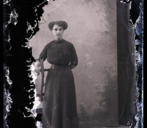 Staand portret van jonge vrouw in lange feestkledij met lange halsketting en golvend gekruld opgestoken haar, Melle, 1910-1920