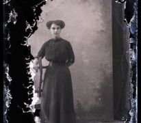 Staand portret van jonge vrouw in lange feestkledij met lange halsketting en golvend gekruld opgestoken haar, Melle, 1910-1920 Staand portret van jonge vrouw in lange feestkledij met lange halsketting en golvend gekruld opgestoken haar, Melle, 1910-1920