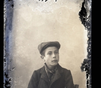 Zittend portret van jonge man in feestkledij met vest en sjaal om de hals, pet op het hoofd, Melle, 1910-1920
