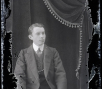 Zittend portret van jonge man in feestkledij met kostuum en witte hemdskraag met stropdas, kuifvormig naar links gekamd haar, Melle, 1910-1920