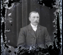 Zittend portret van man in feestkledij met witte hemdsboord en stropdas, gemodelleerde snor en en strak naar rechts gekamd haar, Melle, 1910-1920 Zittend portret van man in feestkledij met witte hemdsboord en stropdas, gemodelleerde snor en en strak naar rechts gekamd haar, Melle, 1910-1920