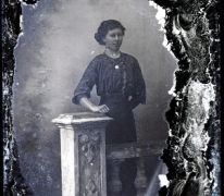 Staand portret van jonge vrouw in feestkledij bestaande uit lange rok en bloes met driekwart mouwen en witte halskraag, halsketting met muntstuk, Melle, 1910-1920