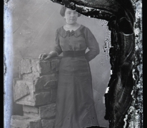 Staand portret van jonge vrouw in feestkledij bestaande uit lang kleed met brede heupband en driekwart mouwen, opgestoken haar, Melle, 1910-1920